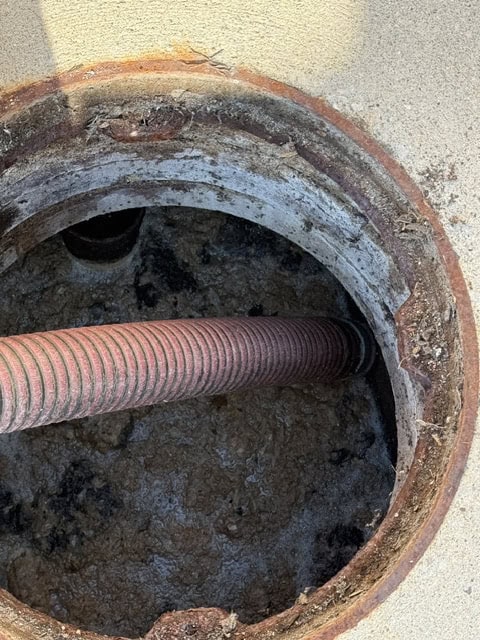 Septic tank cleaning: vacuum hose removing sludge from an open septic tank