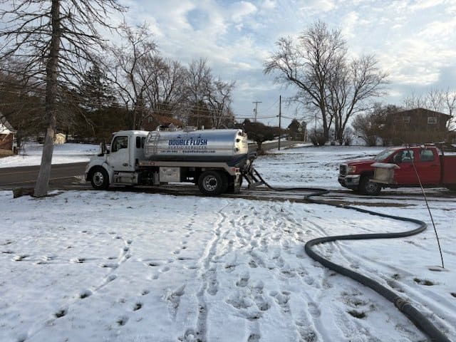 Septic tank pumping in winter: Double Flush Septic truck with hose run across a snowy yard in Northeast Ohio